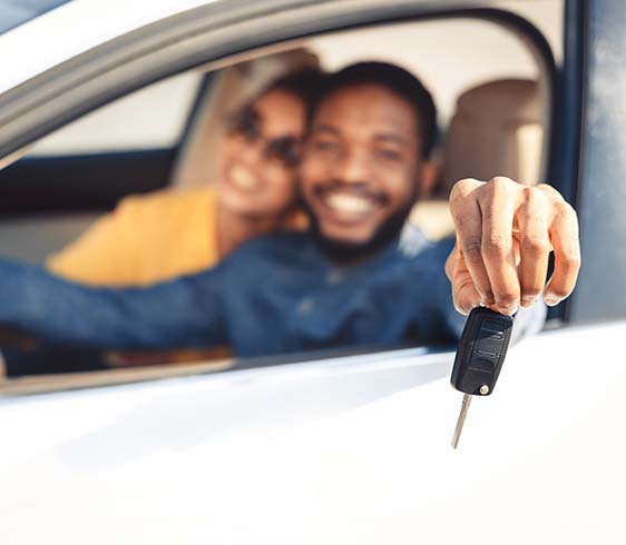 A smiling couple in the front sear of a car with the key in the driver's hand